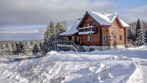 A log cabin with a balcony, surrounded by snow-covered trees and a clear sky. - Stunning Log Chalet - Private Hot Tub, Pool Table, Fireplace (Labelle)