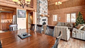 A log cabin interior with a dining area, fireplace, and a Christmas tree. - Stunning Log Chalet - Private Hot Tub, Pool Table, Fireplace (Labelle)