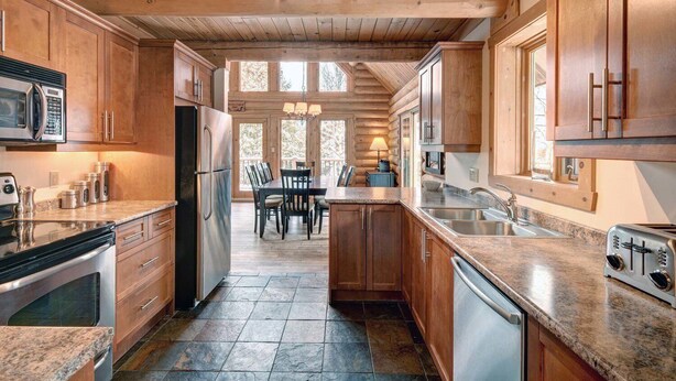A spacious kitchen with wooden cabinets, granite countertops, and a central island. - Stunning Log Chalet - Private Hot Tub, Pool Table, Fireplace (Labelle)