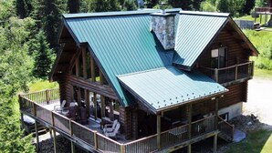 A log cabin with a green metal roof, a balcony with outdoor seating, and a stone chimney. - Stunning Log Chalet - Private Hot Tub, Pool Table, Fireplace (Labelle)