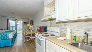 A compact hotel room with a kitchenette, a dining area, and a balcony with a view.