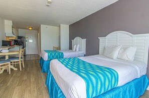 A room with two beds, a desk, and a kitchenette.