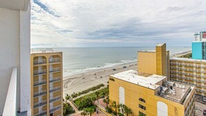 A coastal view with a beach, a high-rise building, and a yellow building with a flat roof.