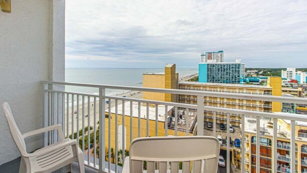 A balcony with a view of the beach and cityscape, including a tall blue building and a yellow building.
