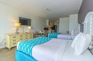 Habitación de hotel con dos camas, un escritorio, una silla, un televisor y una kitchenette.