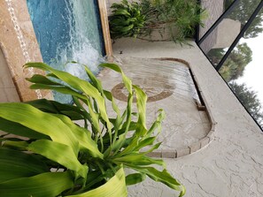 Un espace piscine agrémenté d’un élément décoratif aquatique, entouré de plantes en pot et doté d’un sol carrelé.