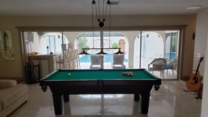 A pool table in a well-lit room with a view of a swimming pool through large glass doors.