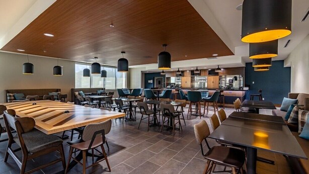 Un restaurant moderne avec un plafond en bois, des tables rondes et des luminaires suspendus noirs.