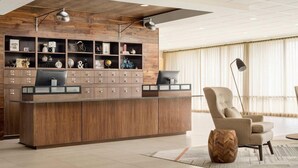 Un comptoir d’accueil moderne avec un revêtement en panneaux de bois et de nombreux tiroirs de rangement, un fauteuil confortable et une grande fenêtre avec des rideaux.