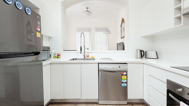 A modern kitchen with white cabinetry, a stainless steel refrigerator, a dishwasher, and a coffee maker. - Stunning Sydney Home 1 (Millers Point)