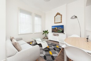 A modern living room with a sofa, a glass coffee table, a dining table, a TV, and a plant. - Stunning Sydney Home 1 (Millers Point)