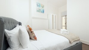 A neatly made bed with white linens and a grey headboard, a white wardrobe, and a framed artwork on the wall. - Stunning Sydney Home 1 (Millers Point)