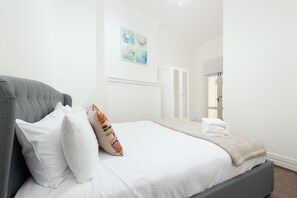 A neatly made bed with white linens and a grey headboard, a white wardrobe, and a framed artwork on the wall. - Stunning Sydney Home 1 (Millers Point)