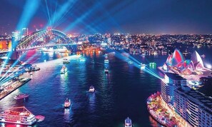 A nighttime cityscape with a prominent bridge, a waterfront area, and illuminated buildings including a recognizable opera house.