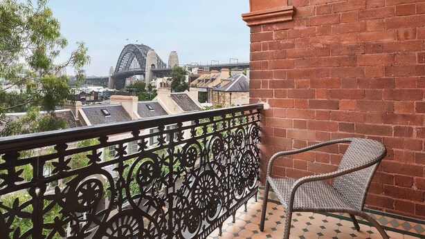 Un balcon orné d’une balustrade en fer forgé, une chaise en osier et une vue sur un pont et des immeubles.