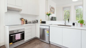 Eine moderne Küche mit weißen Schränken, einem eingebauten Ofen, einem Geschirrspüler und einem Fenster mit Blick auf Grünfläche.