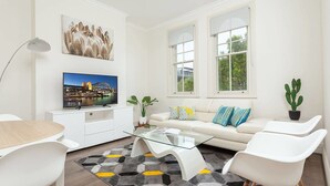 Un salon moderne avec un canapé, une table basse en verre, un téléviseur et une plante, un cactus.