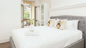 Une chambre à coucher avec une tête de lit rembourrée de couleur grise, une literie blanche et deux oreillers ornés d’un motif d’abeilles.