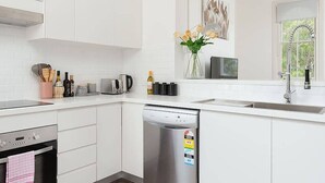 Une cuisine moderne avec des meubles blancs, un four encastré, un lave-vaisselle et une fenêtre donnant sur un espace verdoyant.