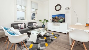 A modern living room with a sofa, coffee table, and chairs, a flat-screen TV, and a large window with a cityscape view. - Stunning Sydney Home 8 (Millers Point)