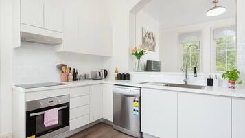 A modern kitchen with white cabinetry, a built-in oven, a dishwasher, and a window with a view of greenery.