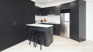 A modern kitchen with dark cabinetry, a stainless steel refrigerator, a central island with stools, and a white countertop. - Ultimate Bondi Living (Bondi Beach)