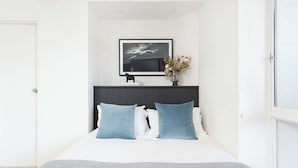 A bedroom with a bed, a framed picture on the wall, and a vase with flowers. - Ultimate Bondi Living (Bondi Beach)