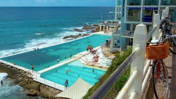 A coastal hotel with a large pool area, a view of the ocean, and a building with signage for 'Bondi Icebergs'. - Ultimate Bondi Living (Bondi Beach)