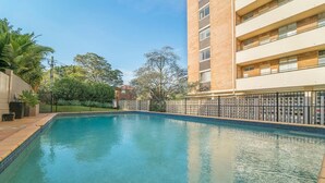 A swimming pool surrounded by a fence, with a building in the background. - Bright and Sunny Studio Apartment (Neutral Bay)