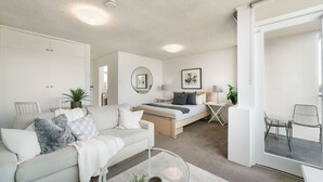 A modern, well-lit living room with a sofa, coffee table, and a bed with a desk. - Bright and Sunny Studio Apartment (Neutral Bay)