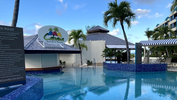 A pool area with a sign for 'Cabana Beach Bar & Restaurant' and a pool deck with lounge chairs. - Beachfront, ground level condo, steps away from beach, pool and relaxation! (Cole Bay)