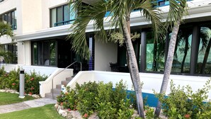 A modern building with a white exterior, large windows, and a stone pathway leading to the entrance. - Beachfront, ground level condo, steps away from beach, pool and relaxation! (Cole Bay)