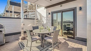 A covered outdoor patio with a round table and wicker chairs, a grill, and a view of a building with a spiral staircase.