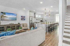 Un salon moderne comprenant un canapé, une table basse et un téléviseur. On y trouve également un coin cuisine avec un réfrigérateur, une table à manger avec des chaises et un îlot de cuisine.