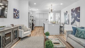 A modern kitchen with white cabinets, a central island, and a dining area with a grey sofa and a coffee table.