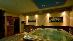 Un cuarto de spa con hidromasaje, paneles de madera, pared de piedra e iluminación empotrada en el techo.