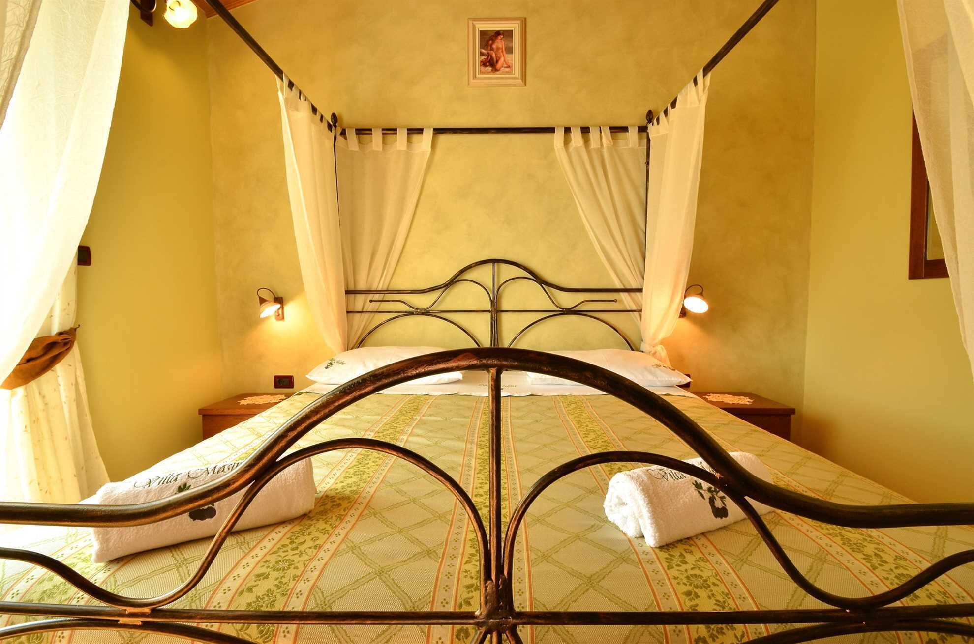 Ein Bett mit Metallgestell, weißen Vorhängen und zwei Nachttischlampen.