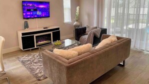 Ett vardagsrum med en platt-TV, en soffa, ett soffbord och en öppen spis.