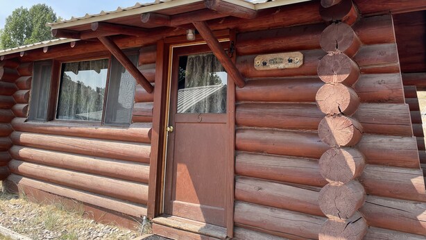 A log cabin with a wooden door, windows, and a wooden sign. - Cozy Log Cabin #5 on Beautiful Canyon Ferry Lake (Helena)