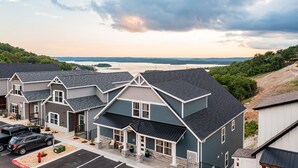 A row of modern, two-story houses with a parking lot in front, set against a backdrop of a lake and hills. - Large-group Retreat w/Hot Tub, 2 Kitchens, Grill (Branson)