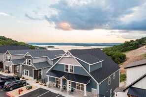 A row of modern, two-story houses with a parking lot in front, set against a backdrop of a lake and hills. - Large-group Retreat w/Hot Tub, 2 Kitchens, Grill (Branson)