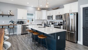 A modern kitchen with white cabinets, stainless steel appliances, and a central island with bar stools. - Large-group Retreat w/Hot Tub, 2 Kitchens, Grill (Branson)