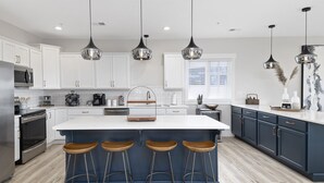 A modern kitchen with white cabinets, a central island with stools, stainless steel appliances, and pendant lighting. - Stunning Lake Views, Pool, Dream Kitchen, Grill (Branson)