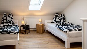 Ett litet, modernt sovrum med två sängar, ett takfönster, ett element och ett litet bord med en lampa.