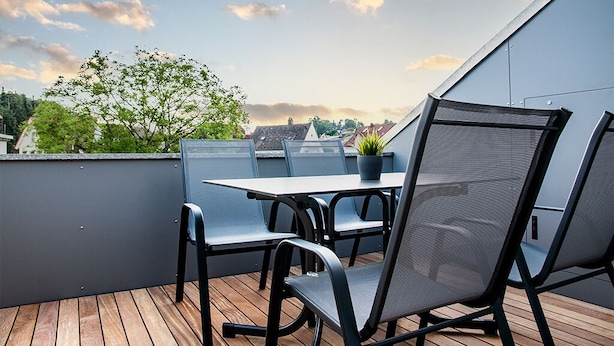 En takterrass med ett bord och stolar, en krukväxt och utsikt över stadsbilden.