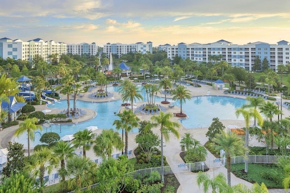 Un resort con varias piscinas, palmeras y un gran complejo de edificios al fondo.