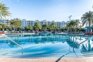 A swimming pool with lounge chairs, palm trees, and a hotel building in the background.