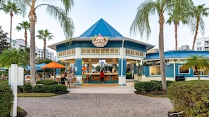 Un Tiki Grill con techo azul, rodeado de palmeras y mesas al aire libre.
