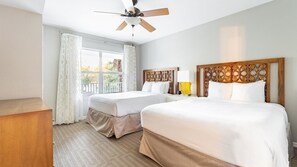 A hotel room with two beds, a ceiling fan, a window with curtains, and a wooden headboard.