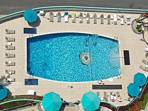 Une piscine rectangulaire avec un îlot central, entourée de chaises longues et de parasols.